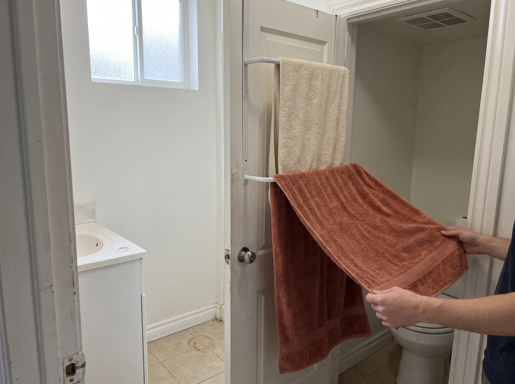 Person hangs a brown towel on an over-door rack in a narrow bathroom.
