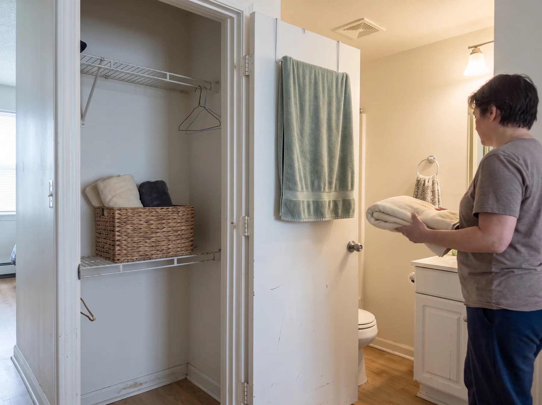 Person carries folded towels from an open bedroom closet toward a bathroom drying rack.