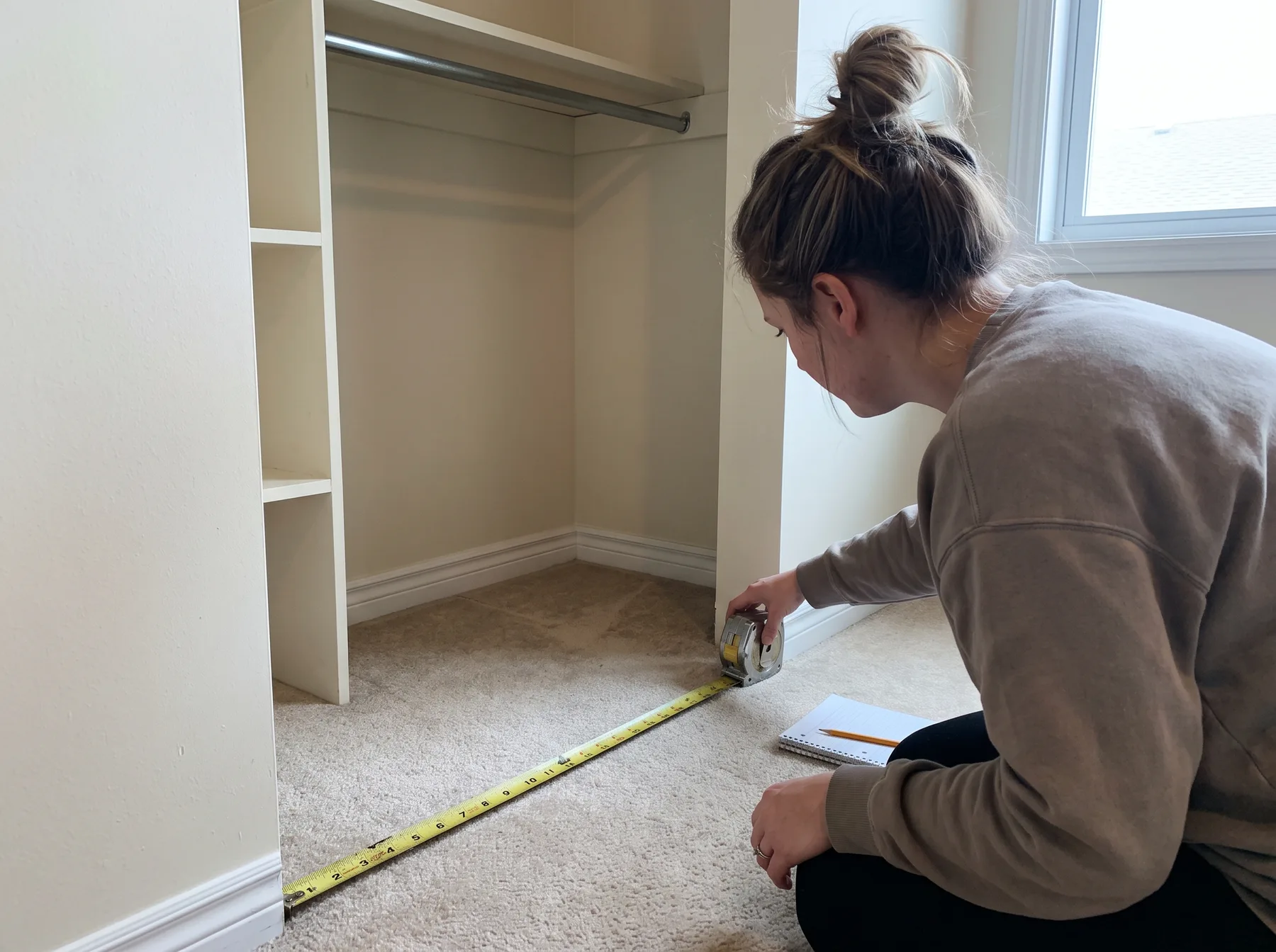 Renter measures an empty closet's width with tape stretched across the carpeted floor.