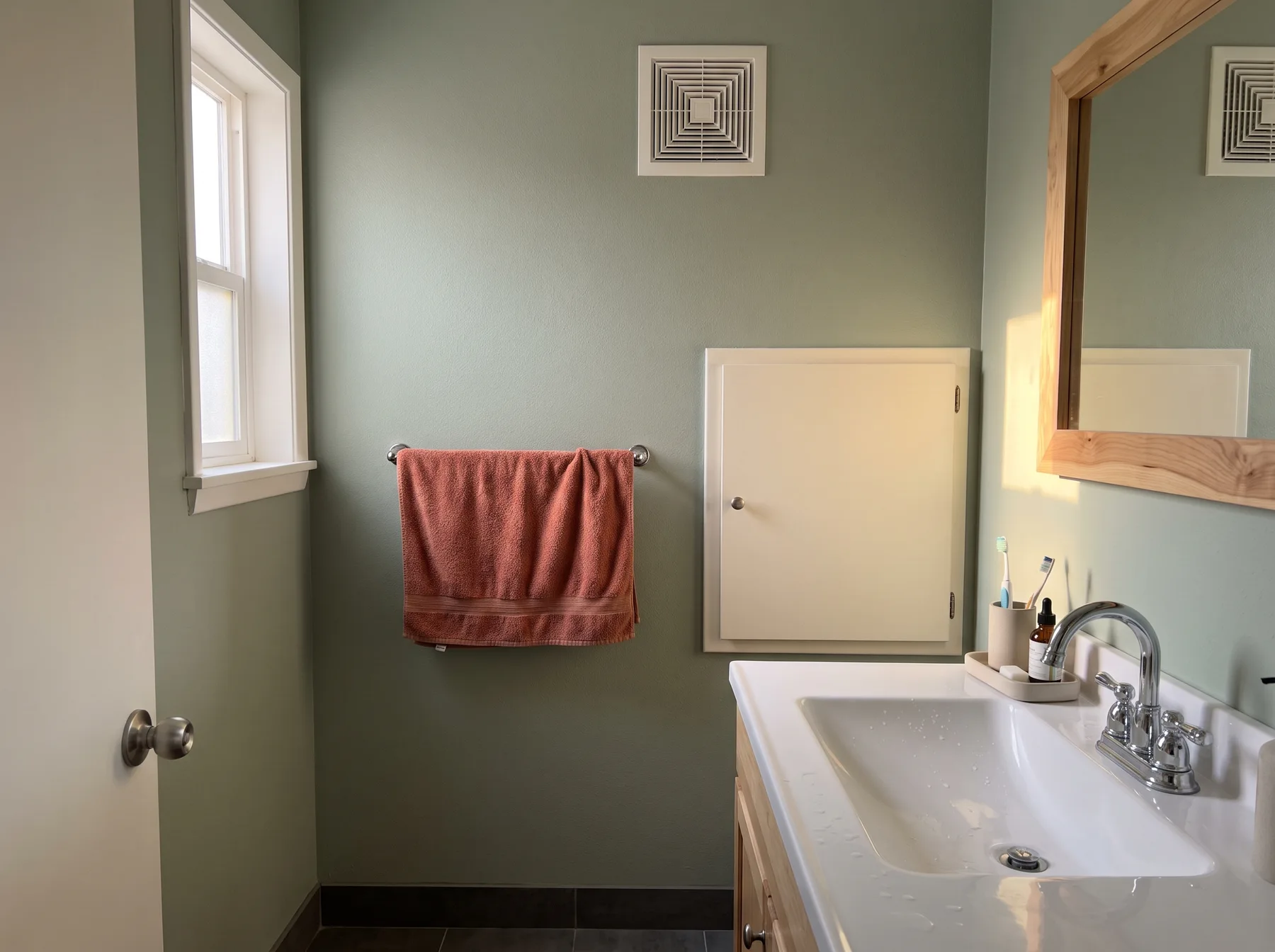 Closed wall cabinet and uncovered exhaust vent sit beside a bathroom sink.